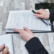 Free Close-up of hands analyzing insurance policy paperwork with pen on table. Stock Photo